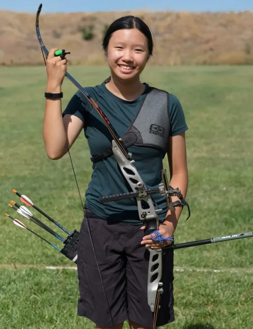 Lily posing with her archery gear in a field
